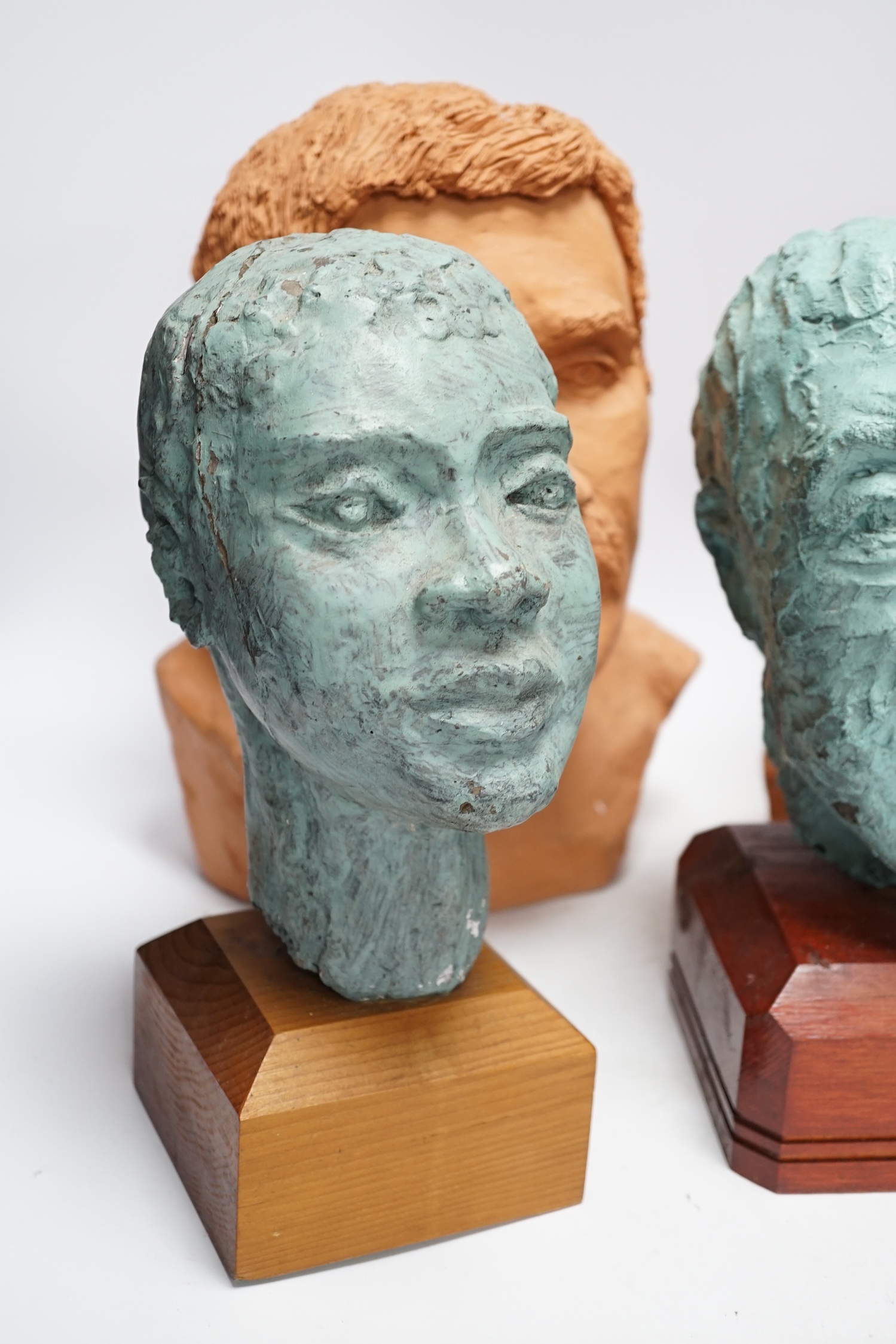 Four art pottery sculpted heads on stands, two terracotta and two painted verdigris green, largest 34cm high